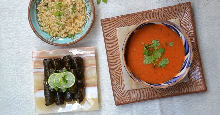 Colorful Fayoum bowls are filled with rice and tomato soup alongside an alabaster dish filled with stuffed vine leaves. Alabaster and Fayoum pottery are some of the best souvenirs from Egypt.